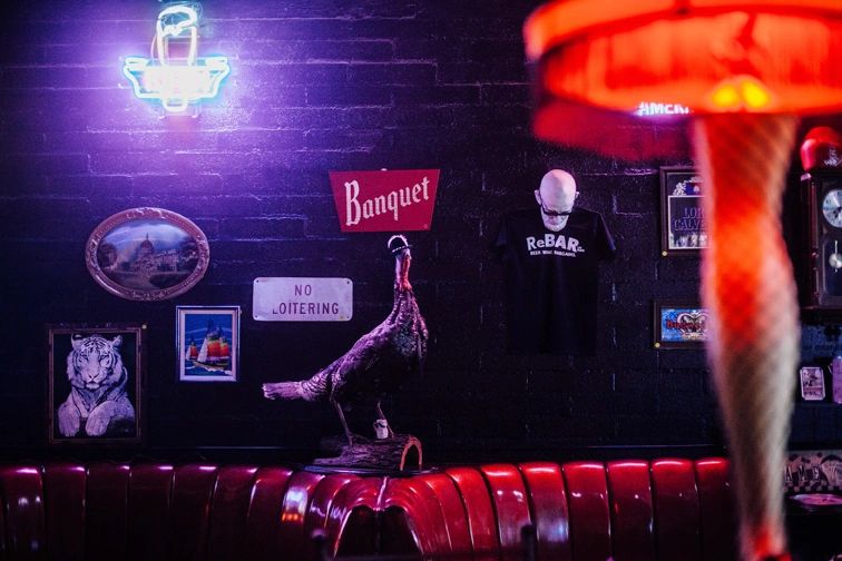 A 'Banquet' sign and a taxidermy turkey perched on a red vinyl booth amid vintage curios at ReBAR
